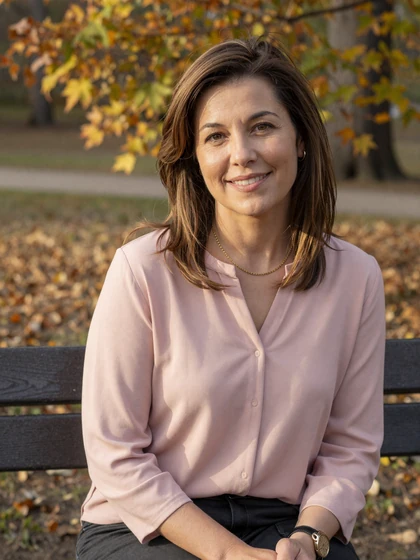 Linda, 46, mature Datempire member smiling on a park bench in autumn light